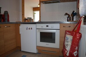 A compact kitchen with a refrigerator, oven, and wooden cabinets. - 2nd floor, view mountain, tv, 58m², Le Grand Bornand (Le Grand-Bornand)