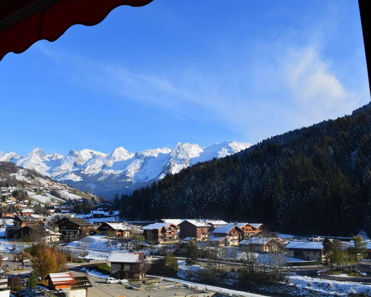 A snow-covered village with traditional wooden houses, a mountain backdrop, and a clear blue sky.
