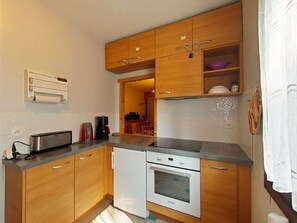 Une cuisine compacte avec des meubles en bois, un four encastré et un plan de travail sur lequel se trouvent un grille-pain et une machine à café.