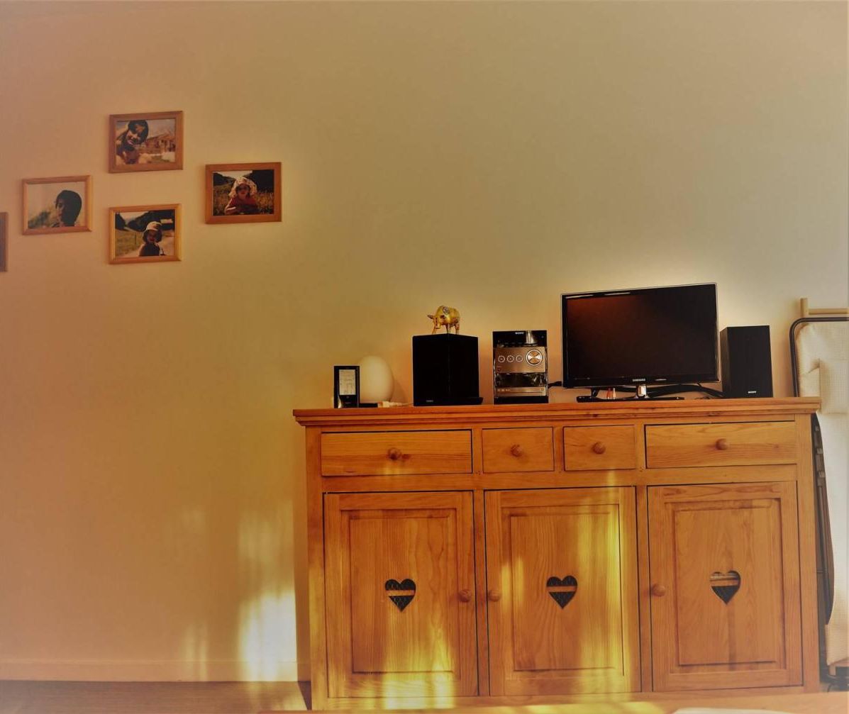A wooden cabinet with heart-shaped cutouts, a television, a coffee maker, and framed pictures on the wall.