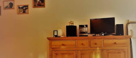 A wooden cabinet with heart-shaped cutouts, a television, a coffee maker, and framed pictures on the wall.