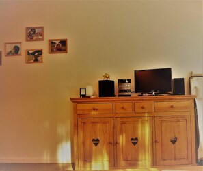 A wooden cabinet with heart-shaped cutouts, a television, a coffee maker, and framed pictures on the wall.