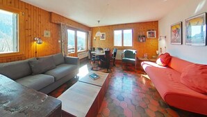 A cozy living room with a wooden interior, a red sofa, a grey sofa, and a dining area with a table and chairs.