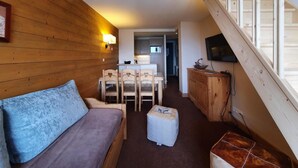 A cozy room with a wooden floor, a sofa, a dining table with chairs, a small ottoman, and a wooden cabinet. - 10m from ski slopes, 5th floor, view mountain, balcony, tv, ski locker, 65m², Montchavin La Plagne (Bellentre)