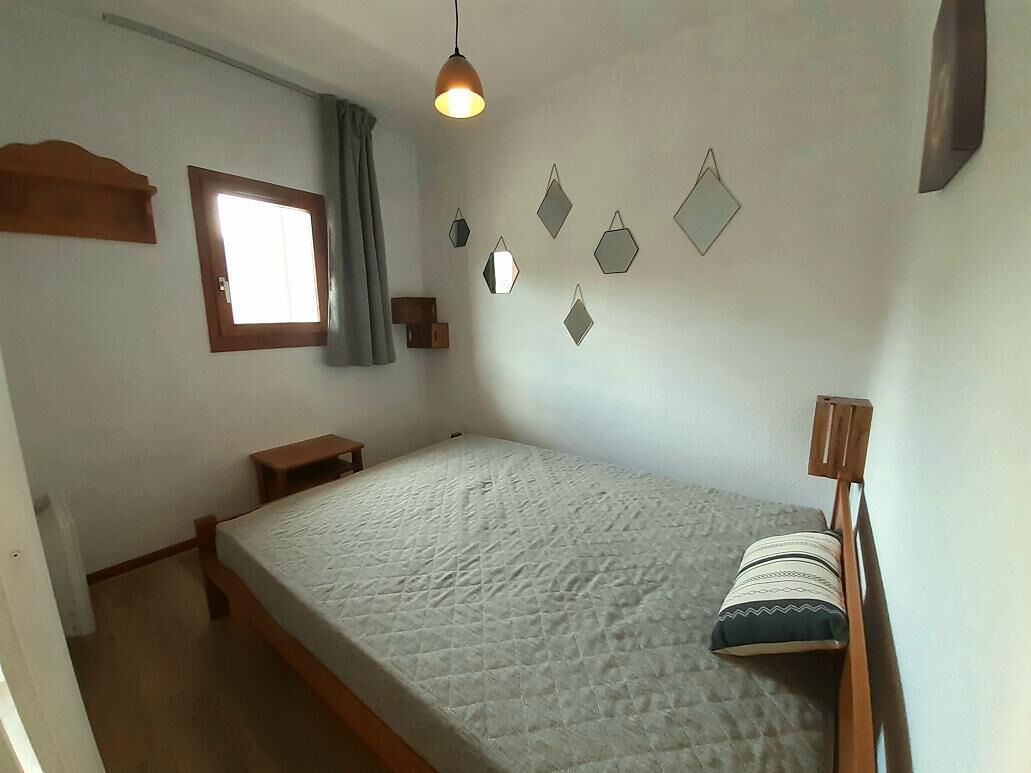 A bedroom with a bed, a window, a bedside table, a hanging light, and wall decorations.