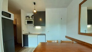 A compact kitchen with a microwave, oven, and sink, a wooden dining table with chairs, and a hanging light fixture. - 70m from ski slopes, 1st floor, view ski slopes, balcony, ski locker, 25m², La Plagne (La Plagne)