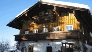 A wooden chalet with a balcony, a snow-covered roof, and a clear blue sky. - One-room apartment 20sqm, shower/WC, kitchenette, balcony (Reit im Winkl)