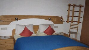 A wooden bed with a blue bedspread, two red pillows, and a wooden headboard. - One-room apartment 20sqm, shower/WC, kitchenette, balcony (Reit im Winkl)