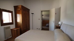 A bedroom with a large bed, a wardrobe, a radiator, a window, and an open door leading to another room. - 50m from ski lifts, 1st floor, terrace, parking, tv, 50m², Montgenèvre (Montgenèvre)