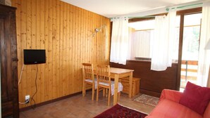 A wooden-paneled room with a dining table and chairs, a television mounted on the wall, and a red sofa. - 50m from ski lifts, 1st floor, terrace, parking, tv, 50m², Montgenèvre (Montgenèvre)