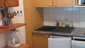 Una cocina compacta con armarios de madera, microondas integrado, cafetera y lavavajillas.