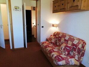 Een gezellige kamer met een gewatteerde bank, houten kasten en een gang naar een andere kamer.
