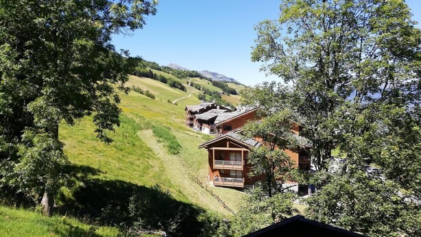 A chalet-style building with a balcony, surrounded by lush greenery and hills in the background. - 3rd floor, balcony, ski locker, 27m², Valmorel (Valmorel)
