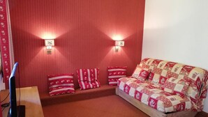 A cozy room with a red carpet, a wooden bench, a sofa with patterned cushions, and two wall-mounted lights. - 3rd floor, balcony, ski locker, 27m², Valmorel (Valmorel)