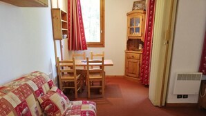 A cozy room with a quilted sofa, a wooden dining table with chairs, a cabinet, and a radiator. - 3rd floor, balcony, ski locker, 27m², Valmorel (Valmorel)