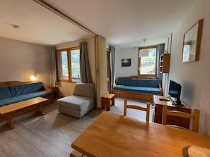 A cozy room with a sofa, a small table, a desk with a chair, and a bunk bed with a blue mattress. - 100m from ski slopes, 3rd floor, balcony, ski locker, 27m², Valmorel (Valmorel)