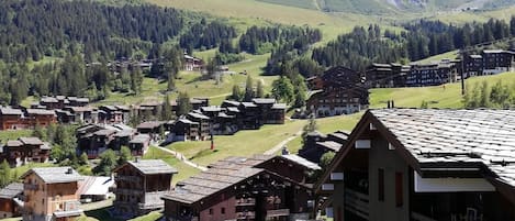 A mountainous village with traditional wooden buildings, a ski lift, and a backdrop of forested hills.