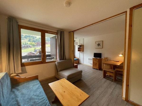 A room with a sofa, a wooden table, a TV, and a dining area with chairs.