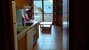 A kitchen with wooden cabinets, a countertop, a sink, and a stove. There is a window with a view of a house and a metal roof. - Ground floor, balcony, ski locker, 35m², Pra Loup (Pra Loup)