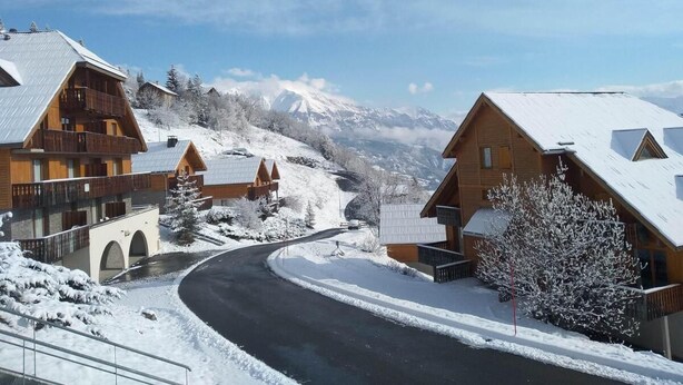 A snow-covered village with wooden buildings, a curved road, and a mountain in the background. - Ground floor, balcony, ski locker, 35m², Pra Loup (Pra Loup)
