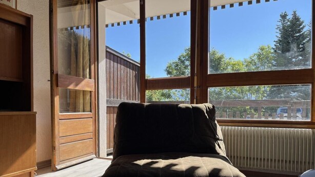 A room with a bed, a wooden cabinet, and a window with a view of trees and a building. - Ground floor, balcony, tv, 30m², Pra Loup (Pra Loup)