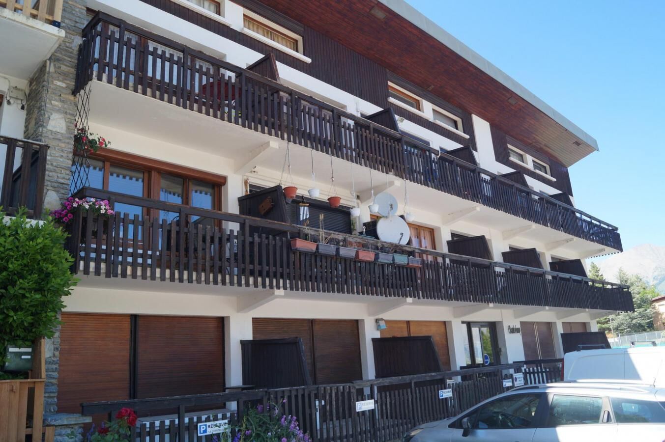 Ein mehrstöckiges Hotel mit Balkonen, ein Auto vor der Fassade und ein Berg im Hintergrund.