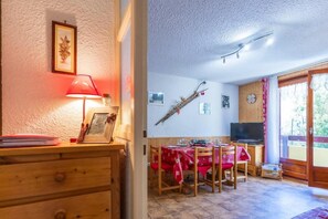 A cozy dining area with a wooden table set for four, a television, and a window with curtains. - 1st floor, balcony, ski locker, 33m², Valloire (Valloire)