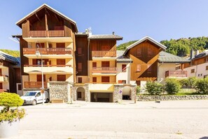 A multi-story wooden building with balconies, a stone entrance, and a parking area. - 1st floor, balcony, ski locker, 33m², Valloire (Valloire)