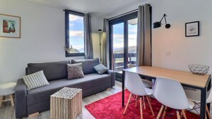 A modern living room with a grey sofa, white chairs, a wooden dining table, and a red rug.