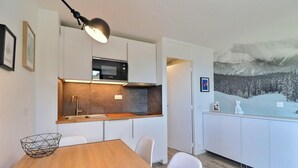 A modern kitchen with white cabinets, a wooden dining table, and a painting of a snowy landscape.