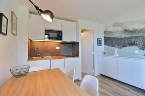 A modern kitchen with white cabinets, a wooden dining table, and a painting of a snowy landscape.