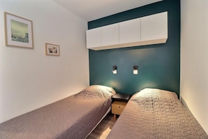 A bedroom with two single beds, a nightstand, a wall-mounted cabinet, and two wall-mounted light switches.