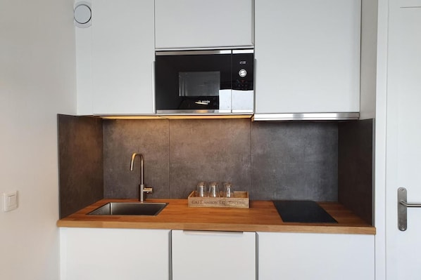A compact kitchen with a Bosch microwave, a stainless steel sink, and a wooden countertop.