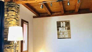 Una sala de estar acogedora con pared de piedra, vigas de madera en el techo, un sofá, una lámpara y una frase motivacional en la pared.