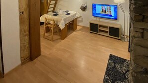 Una habitación acogedora con cama tipo altillo, una mesa de comedor con sillas, un televisor y una pared de piedra.