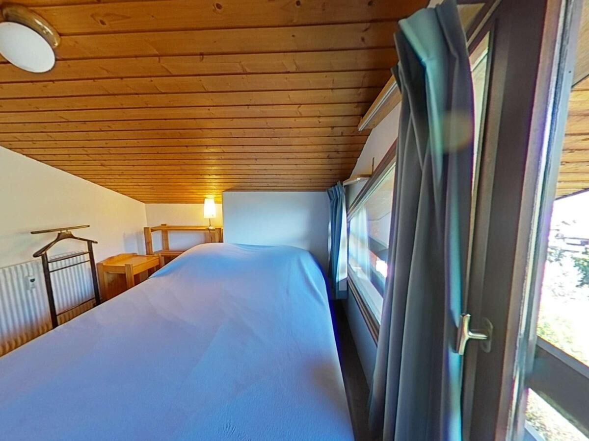 A single bed in a room with a wooden ceiling, a small table, and a lamp.