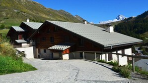 A chalet-style building with a sloped roof, a covered porch, and a gravel driveway.