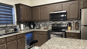 A modern kitchen with dark brown cabinets, a granite countertop, stainless steel appliances, and a built-in dishwasher. - Cozy Family-sized Townhome (Pharr)
