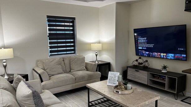 A modern living room with a beige sofa, a coffee table, a flat-screen TV, and a TV stand with a decorative plant. - Cozy Family-sized Townhome (Pharr)