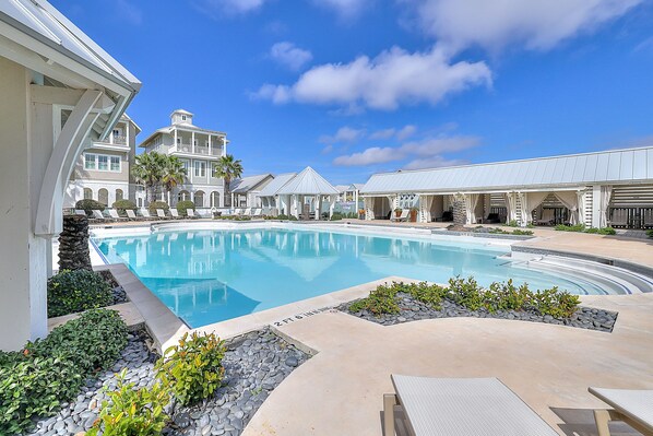 A pool area with lounge chairs, a large pool, and a building with balconies.