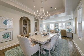 A dining area with a chandelier, white chairs, and a table set for six.