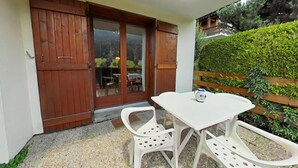 En terrasse med hvidt bord og stole, en trædør og udsigt til en grøn hæk.