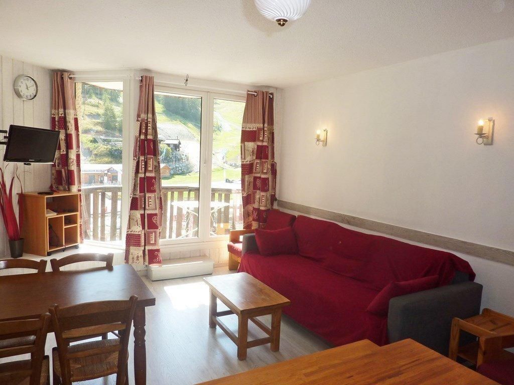 A living room with a red sofa, wooden furniture, a television, and a window with curtains.