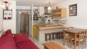 Een compacte leefruimte met een rode bank, een houten eettafel en stoelen. Een keuken is zichtbaar met een magnetron, broodrooster en kastjes.