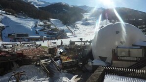 Een besneewd berggebied met een grote, bolvormige structuur, mogelijk een opslagtank, en een skilift op de achtergrond.