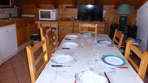 A dining area with a table set for four, wooden chairs, a television, and a microwave in the background. - 4th floor, balcony, parking, tv, ski locker, 55m², Saint Gervais (Saint-Gervais-les-Bains)