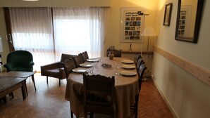 Un coin repas avec une table ronde dressée pour six personnes, entourée de chaises, d’un fauteuil vert et d’une table en bois.