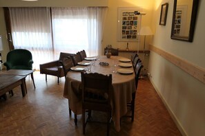 Comedor con una mesa redonda dispuesta para seis personas, rodeada de sillas, un sillón verde y una mesa de madera.