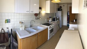 Une cuisine avec des meubles blancs, un évier à deux bacs, une cuisinière et un réfrigérateur.