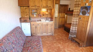 A compact kitchen with wooden cabinets, a refrigerator, and a patterned sofa. - 300m from ski slopes, 1st floor, view mountain, balcony, parking, tv, 28m², Saint Gervais (Saint-Gervais-les-Bains)